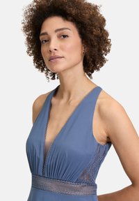 Niebieska sukienka bez rękawów z głębokim dekoltem w kształcie litery V, przezroczystymi koronkowymi akcentami po bokach oraz teksturowanym wykończeniem w pasie. Gładkie wykończenie tkaniny.