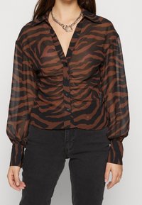 Blusa trasparente marrone e nera con motivo a strisce di tigre, con chiusura frontale a bottoni e maniche lunghe leggermente a sbuffo.