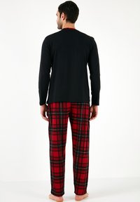 Herrepyjamas med en langærmet sort top og røde ternede bukser. Bukserne har en blød tekstur med sorte og hvide detaljer i mønsteret.