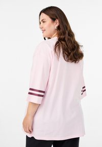 Svetloružové bavlnené tričko s krátkymi rukávmi, zdobené dvoma bordovými pruhmi na lemoch. Voľný strih a okrúhly výstrih.