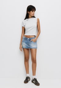 T-shirt gris court à manches courtes, jupe en denim bleu mini avec poches, et baskets marron avec des accents blancs. Fond blanc.