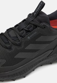 Primo piano di una scarpa da trail running nera Gore-Tex Terrex con suola testurizzata, lacci e fodera interna rossa visibile.