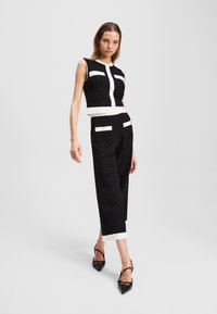 Black textured two-piece outfit with a sleeveless top and high-waisted, cropped pants, featuring white accents and a fitted design.