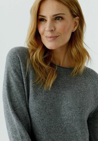 Pull en maille gris avec une coupe décontractée, un col rond et des détails côtelés sur les épaules. Texture douce et tissu léger.