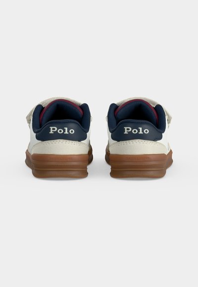 Ζευγάρι λευκά και ναυτικά Polo sneakers με καφέ σόλες, εμφανιζόμενα από πίσω σε απλό ανοιχτό φόντο.