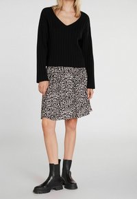 Sort ribbet sweater med V-hals parret med en kort, mønstret nederdel i sort og hvid. Modellen bærer sorte ankelstøvler med kraftige såler.