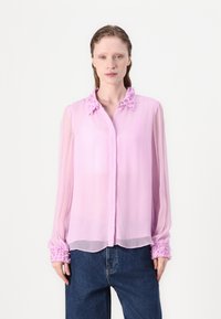 Helle rosa Bluse aus durchscheinendem Stoff mit Rüschensaum, gerafftem Kragen und elastischen Bündchen. Das Hemd hat eine Knopfleiste und einen lockeren Schnitt.
