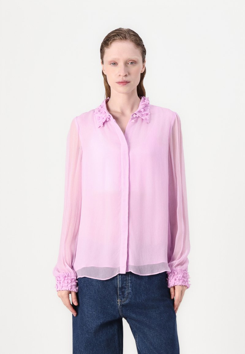 Helle rosa Bluse aus durchscheinendem Stoff mit Rüschensaum, gerafftem Kragen und elastischen Bündchen. Das Hemd hat eine Knopfleiste und einen lockeren Schnitt.