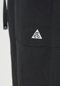 Μαύρο παντελόνι με τρίγωνο λευκό λογότυπο "acg". Υλικό με υφή, καθαρός σχεδιασμός και απλή, στενή γραμμή. Μινιμαλιστικό στυλ.