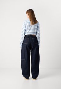 Maglietta a righe blu chiaro e bianca a maniche lunghe abbinata a pantaloni larghi in denim scuro. I pantaloni presentano due tasche posteriori e una vita.