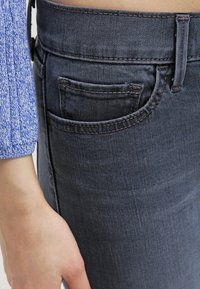 Vaqueros gris oscuro con una textura suave, que cuentan con un bolsillo trasero, costuras contrastadas y una cinturilla segura, combinados con una blusa de punto azul.