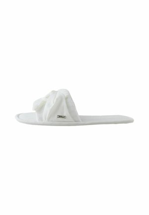 Fehér, párnázott, nyitott orrú papucs, csavart szövetpánttal és egy kis fém márkajelzéssel az oldalon, oldalnézetben mutatva.