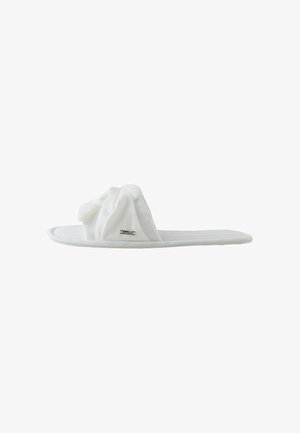 Zapatilla blanca acolchada con puntera abierta, con una tira de tela torcida y una pequeña etiqueta metálica de la marca en el lateral, mostrada de perfil.