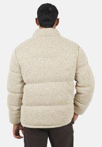 Giacca puffer beige con finitura testurizzata, caratterizzata da un colletto alto e sezioni imbottite. La vista posteriore mette in evidenza il design voluminoso.