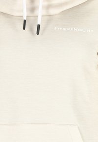 Beżowa bluza z kapturem, białymi sznurkami, czarnymi końcówkami i logo „Swedemount” białym tekstem w górnej lewej części klatki piersiowej. Brak widocznej osoby.