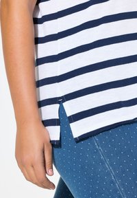 Witte en marineblauwe gestreepte top met een zijsplit, gemaakt van zachte stof, gecombineerd met blauw met stippen leggings, die een gladde textuur tonen.