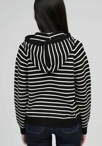 Hoodie à rayures noires et blanches avec une poche avant, des poignets et un ourlet côtelés, doté d'une capuche avec cordon de serrage et d'un design décontracté.