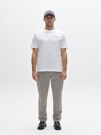 Vitt t-shirt med korta ärmar och svart logotyp, ljusgrå byxor och svarta skor. Personen bär en mörkgrå keps med en logotyp.