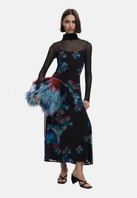 Must lillemustriga kleit läbipaistvate pika varrukaga, millel on värvikad mustrid. Sobitatud kaisus sinise ja punase käekoti ning rihmikujuliste mustade sandaalidega.