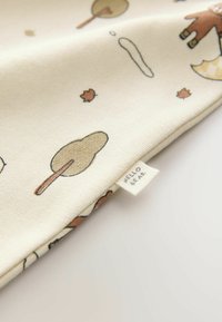 Bawełniana tkanina o jasnobeżowym tle, z ilustracjami w stylu kreskówkowym przedstawiającymi drzewa, liście i niedźwiedzia. Etykieta głosi "WITAJ NIEDŹWIEDZIU".