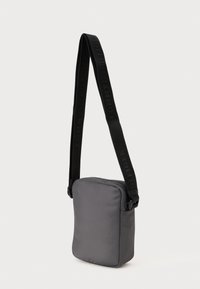 Szara prostokątna torba na ramię wykonana z gładkiego materiału, z czarnym regulowanym paskiem z wytłoczonym logo oraz zamknięciem na zamek błyskawiczny.