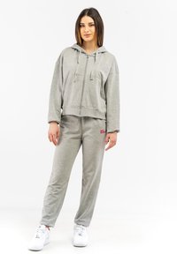 Grauer Zip-Hoodie mit großzügigem Schnitt, kombiniert mit passenden grauen Jogginghosen. Beide Kleidungsstücke bestehen aus einem weichen Stoff mit minimalem Branding.