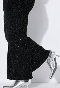 Pantaloni neri con paillettes e orlo svasato, abbinati a stivaletti a tacco argentati lucidi con cerniera laterale.