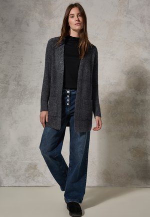 Cardigan tricoté gris charbon avec un devant ouvert, des manches longues et des poches latérales, associé à un jean en denim bleu à jambes larges.