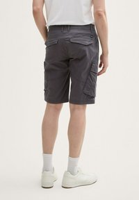 Shorts cargo gris avec poches latérales et poches arrière à patch, fabriqués en tissu léger. Portés avec des baskets blanches et des chaussettes.