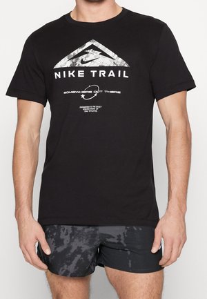 Mann trägt ein schwarzes Nike Trail T-Shirt mit weißem Logo und Schriftzug, kombiniert mit schwarz-grau gemusterten Sportshorts.