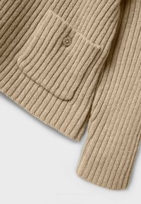 Beige Strickjacke mit vertikalen Rippungen, ausgestattet mit einer aufgesetzten Tasche und einem runden Knopfverschluss. Weiche Textur mit lockerer Passform.