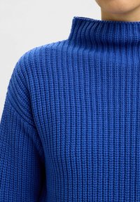 Blauer gerippter Rollkragenpullover mit strukturiertem Strick. Verfügt über einen hohen Kragen und ein Design mit tiefen Schultern, das eine lässige Passform bietet.