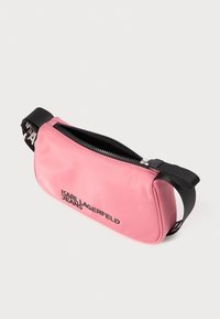 Rozā neilona jostas soma ar rāvējslēdzēju, ar melnu siksnu un "KARL LAGERFELD JEANS" logotipu. Apaļa forma, gluda tekstūra.