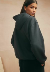 Overmaat, donkergrijze hoodie met een kangaroozak, ribgebreide boorden en zoom. Het materiaal lijkt zacht, met een gladde textuur en een capuchon.