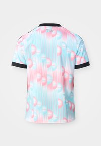 Majica kratkih rukava s crnim ovratnikom i manšetama, s pastelnim ružičasto-plavim geometrijskim uzorkom i tekstom "Ceci n'est pas un maillot" na gornjem dijelu leđa.