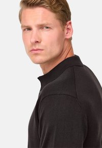 Čierne polo tričko s textúrovaným úpletom, krátkym golierom a trojgombíkovým zapínaním. Model je zobrazený z boku na neutrálnom pozadí.