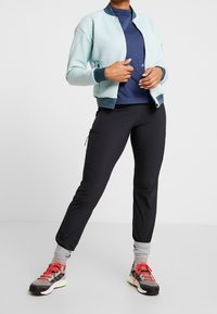 Světle modrá strukturovaná zipová bunda, námořnický top, černé tapered kalhoty, šedé tenisky s neonovými akcenty, červené tkaničky a žebrované manžety na kotník.