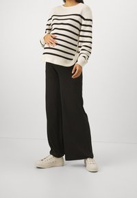 Cream and black striped knit sweater with a round neckline, paired with wide black pants and white sneakers. Smooth texture, relaxed fit.
