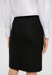 Zwarte kokerrok met een split aan de achterkant, gladde textuur en een getailleerde pasvorm, gecombineerd met een lichtgekleurde blouse met manchetdetails.