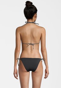 Set di bikini nero con top a collare e spalline decorate, e culotte con lacci regolabili sui lati. Tessuto morbido con un design a copertura minima.