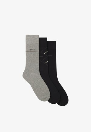 Tre paia di calze in grigio e nero. La calza grigia presenta un logo con una banda, mentre le calze nere hanno un motivo geometrico e un branding.