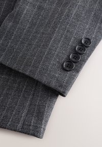 Manche de costume gris à fines rayures avec quatre boutons noirs disposés verticalement près du poignet sur un fond clair.