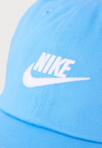 Ανοιχτό μπλε υφασμάτινο καπέλο μπέιζμπολ με λευκό λογότυπο Nike και το χαρακτηριστικό σήμα στη μπροστινή πλευρά.