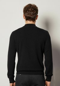 Schwarzer Pullover mit rundem Kragen, langen Ärmeln und figurnaher Passform. Hergestellt aus weichem Material mit glatter Textur.