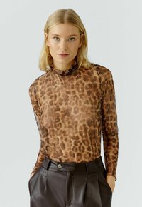 Langarmtop in doorschijnende bruine stof met een panterprint, met een gerimpelde hoge halslijn en een getailleerd silhouet, gecombineerd met donkere broek.