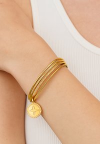 Gold bracelet set featuring three slim bangles with varied textures, including a circular charm with a star design as an accent.