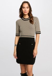 Knit dress featuring a beige patterned top with "M" motif, short sleeves, and a fitted black skirt with two front pockets and silver accents.