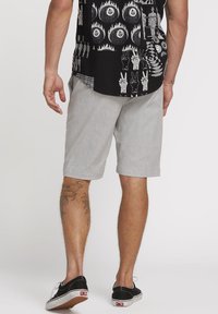 Gray shorts with a subtle texture, hitting just above the knee. Worn with a black graphic printed shirt and black sneakers.