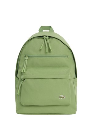 Mochila verde claro con dos compartimentos con cremallera y un pequeño logo de cocodrilo en el bolsillo frontal sobre un fondo blanco.