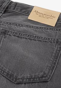 Jeans de mezclilla gris con un bolsillo trasero con costura en contraste y una etiqueta de cuero marrón grabada con "Abercrombie" en la cinturilla.